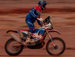 Gerard Farrés conduce una moto de rally con los colores de Macbor, visto de perfil sobre tierra.